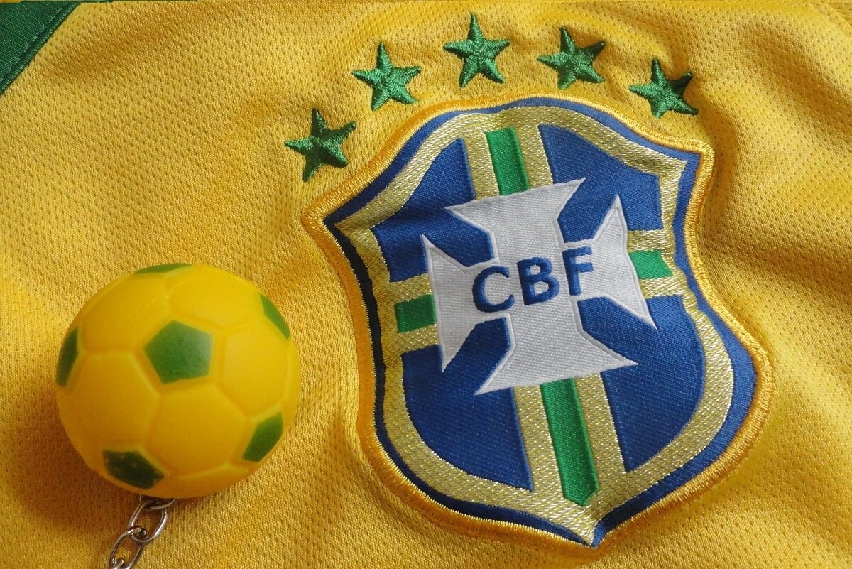 Parte da camisa da Seleção Brasileira de Futebol, mostra o logo da CBF e as 5 estrelas. Ao lado, uma bolinha verde e amarela.